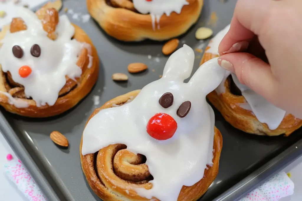 Decorating bunny-shaped cinnamon rolls with icing and candy toppings on a baking tray